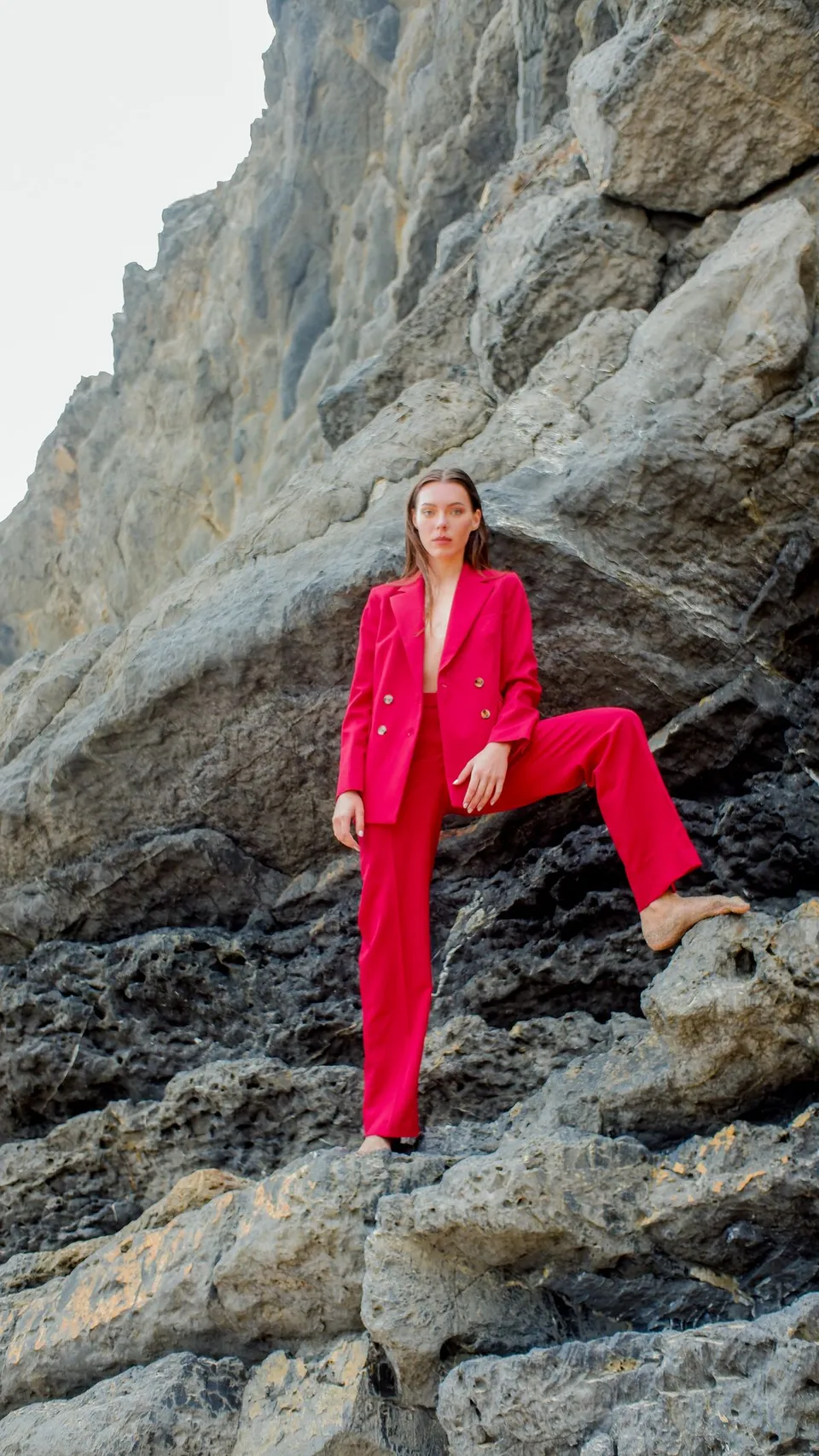 Woman wearing a bright pink tailored suit against a rocky coastal backdrop